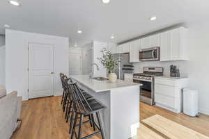 Kitchen with stainless steel appliances, an island with sink, sink, and white cabinets