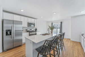 Kitchen with a breakfast bar, sink, appliances with stainless steel finishes, a kitchen island with sink, and white cabinets