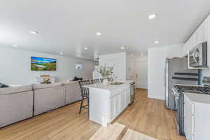 Kitchen featuring white cabinetry, stainless steel appliances, a breakfast bar area, and a center island with sink