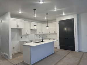 Kitchen featuring pendant lighting, white cabinetry, a kitchen island with sink, and sink