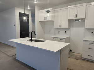 Kitchen with decorative light fixtures, an island with sink, sink, white cabinets, and light stone counters