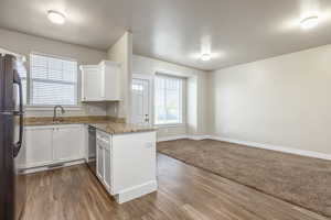 Kitchen featuring black refrigerator, dishwasher, white cabinetry, sink, and kitchen peninsula