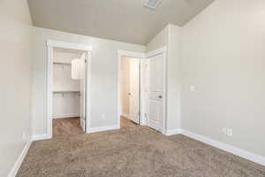 Unfurnished bedroom with a walk in closet, carpet flooring, a closet, and a textured ceiling