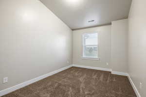 Carpeted spare room featuring vaulted ceiling