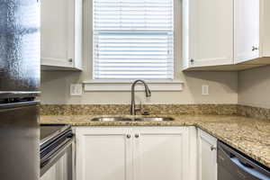 Kitchen featuring white cabinetry, light stone countertops, sink, and black appliances