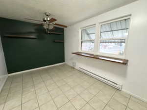 Tiled empty room featuring ceiling fan, a textured ceiling, and baseboard heating