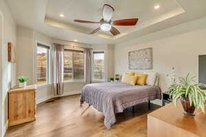 Bedroom with a tray ceiling, light hardwood / wood-style flooring, and ceiling fan