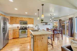 Kitchen with sink, a kitchen island with sink, hanging light fixtures, stainless steel appliances, and light brown cabinets