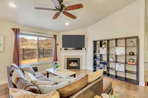 Living room featuring ceiling fan, lofted ceiling, a fireplace, and light hardwood / wood-style flooring