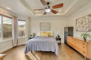 Bedroom with ceiling fan, a tray ceiling, and light wood-type flooring