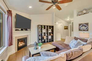 Living room with ceiling fan, lofted ceiling, a fireplace, and light hardwood / wood-style floors