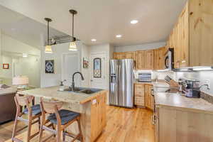 Kitchen featuring sink, hanging light fixtures, light wood-type flooring, light brown cabinets, and appliances with stainless steel finishes