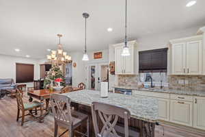 Kitchen featuring sink, a breakfast bar area, decorative light fixtures, light stone countertops, and cream cabinets