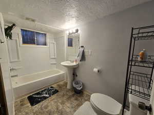 Full bathroom with toilet, shower / bath combination, sink, and a textured ceiling