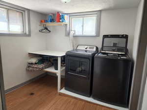 Clothes washing area featuring wood-type flooring, washer and clothes dryer, and a textured ceiling