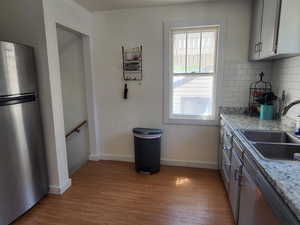 Kitchen with sink, light stone counters, light wood-type flooring, stainless steel appliances, and decorative backsplash