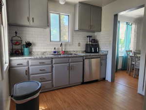 Kitchen featuring sink, light hardwood / wood-style flooring, stainless steel dishwasher, and gray cabinets