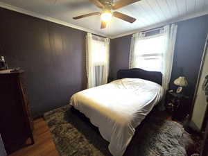 Bedroom featuring crown molding, dark wood-type flooring, wooden walls, and ceiling fan