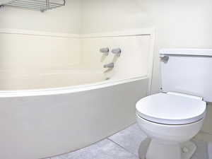 Primary Bathroom with a corner garden bathtub, tile floors, and toilet