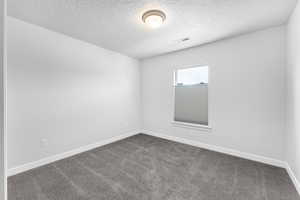 Spare room featuring dark carpet and a textured ceiling