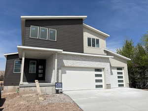Modern home featuring an attached garage, concrete driveway, brick siding, and a porch