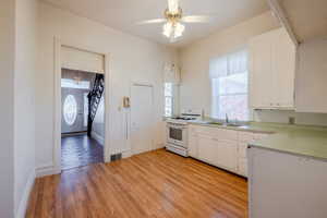 Kitchen featuring white range with gas cooktop, sink, white cabinetry, and light wood-type flooring