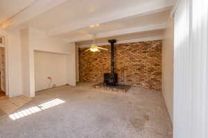 Living room with light colored carpet, beam ceiling, and a wood stove