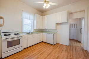 Kitchen with sink, light wood-type flooring, ceiling fan, white appliances, and white cabinets