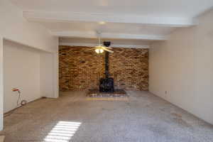 Living room featuring beamed ceiling, a wood stove, and carpet flooring