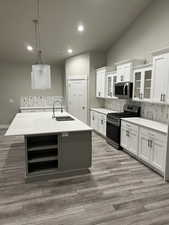 Kitchen featuring appliances with stainless steel finishes, pendant lighting, sink, white cabinets, and a kitchen island with sink