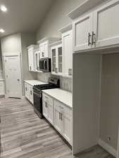 Kitchen featuring white cabinetry, stainless steel appliances, tasteful backsplash, vaulted ceiling, and light wood-type flooring