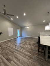 Unfurnished living room with lofted ceiling, ceiling fan with notable chandelier, and dark wood-type flooring