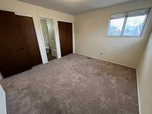 Unfurnished bedroom with connected bathroom and carpet