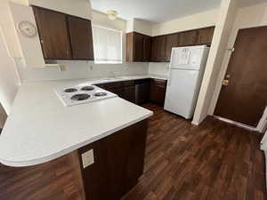 Kitchen with sink, white appliances, dark brown cabinets, dark hardwood / wood-style flooring, and kitchen peninsula