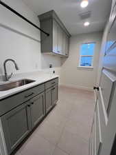 Clothes washing area featuring light tile patterned flooring, sink, cabinets, hookup for a washing machine, and hookup for an electric dryer