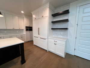 Kitchen with dark hardwood / wood-style floors, tasteful backsplash, white cabinets, stainless steel oven, and light stone countertops