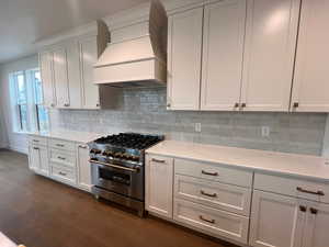 Kitchen with custom exhaust hood, high end range, dark hardwood / wood-style flooring, light stone countertops, and white cabinets