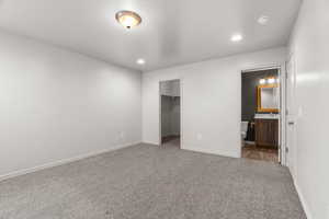 Unfurnished bedroom with a walk in closet, ensuite bathroom, carpet, and a closet