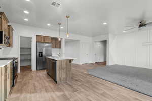 Kitchen with decorative light fixtures, a center island with sink, light hardwood / wood-style flooring, ceiling fan, and stainless steel appliances