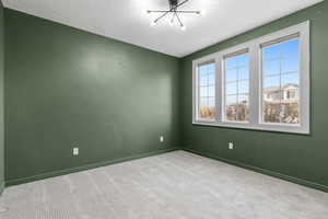 Empty room featuring light colored carpet, a textured ceiling, and a notable chandelier