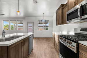 Kitchen with stainless steel appliances, sink, hanging light fixtures, and light wood-type flooring