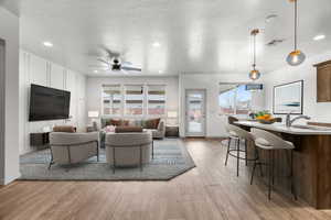 Living room featuring ceiling fan, sink, light hardwood / wood-style flooring, and a textured ceiling