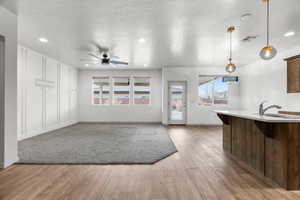 Unfurnished living room featuring ceiling fan, sink, light hardwood / wood-style flooring, and a textured ceiling