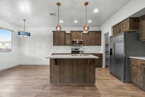 Kitchen with pendant lighting, sink, appliances with stainless steel finishes, dark brown cabinetry, and light hardwood / wood-style floors