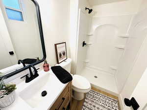 Bathroom with wood-type flooring, toilet, vanity, and a shower