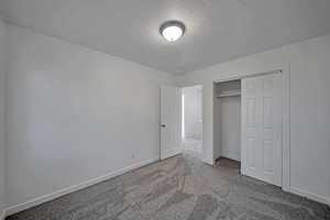 Unfurnished bedroom with carpet floors, a textured ceiling, and a closet