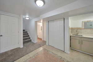 Basement with sink, light colored carpet, electric panel, and a textured ceiling