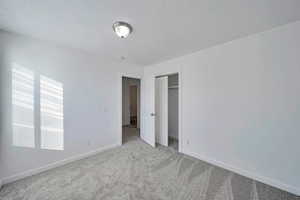 Unfurnished bedroom with light colored carpet, a closet, and a textured ceiling