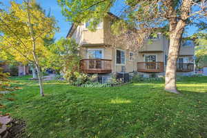 Rear view of house with central AC unit, a lawn, and a deck