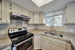 Kitchen featuring white cabinetry, light stone counters, sink, and stainless steel range with electric cooktop